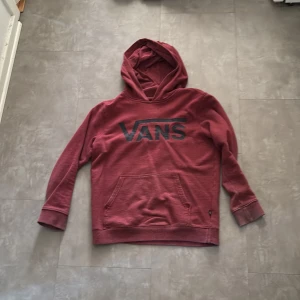 Vinröd hoodie från Vans - Säljer en snygg vinröd hoodie från Vans med stor logga på bröstet. Tröjan har en klassisk känguruficka och en bekväm huva. Perfekt för en avslappnad stil.