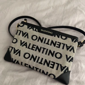 Valentino axelremsväska  - Classy axelväska från Valentino som även går att använda som en clutch, den är grå och svart med en praktisk dragkedja upptill. Den har en justerbar axelrem, dock så har den lite fläckar inuti sig, men det går att ta bort!