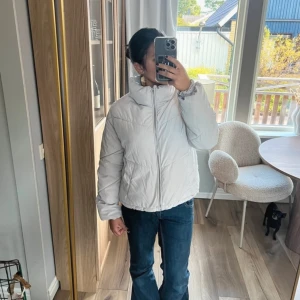 Beige pufferjacka - Säljer en snygg beige pufferjacka med dragkedja och hög krage. Jackan har långa ärmar och är perfekt för kyligare dagar. Den är i en stilren design som passar till det mesta. Perfekt för dig som vill hålla värmen med stil!