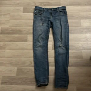 Blå jeansbyxor från tiger of sweden  - Snygga blå jeansbyxor från tiger of sweden i modellen Pistolero. De har en klassisk femficksdesign med slitna detaljer på framsidan. Perfekta för en avslappnad stil.