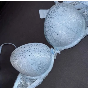 Ljusblå push up spets-bh med strassdetaljer - Elegant ljusblå bh med spets och glittrande strassdetaljer. Den har justerbara axelband och en fin rosett mellan kuporna. Perfekt för att känna sig extra speciell. Har aldrig använt dem. 