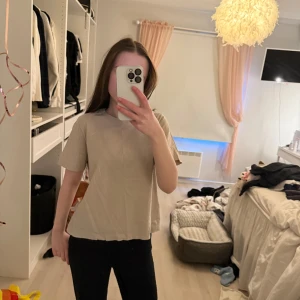 Beige t-shirt - En enkel och stilren beige t-shirt med rund halsringning och korta ärmar. Perfekt för en avslappnad look.
