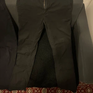 Svarta byxor med dragkedja - Snygga svarta byxor med dragkedja framtill. De har en klassisk design och passar perfekt för en stilren look. Byxorna har en rak passform och är tillverkade i ett bekvämt material.