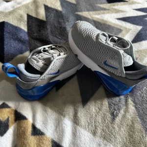 Grå och blå Nike sneakers - Säljer ett par oanvända sneakers från Nike för småbarn i storlek 25. Mitt barn gillade aldrig dom därav oanvända. Säljs för 250kr