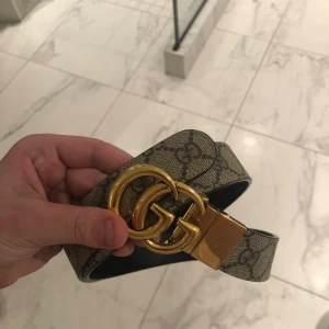 Gucci bälte med GG-spänne - Säljer ett snyggt Gucci bälte i mycket bra skick. Det har ett klassiskt GG-spänne i guld och är gjort av svart skinn. Perfekt för att ge din outfit en lyxig touch. Passar både till vardag och fest!
