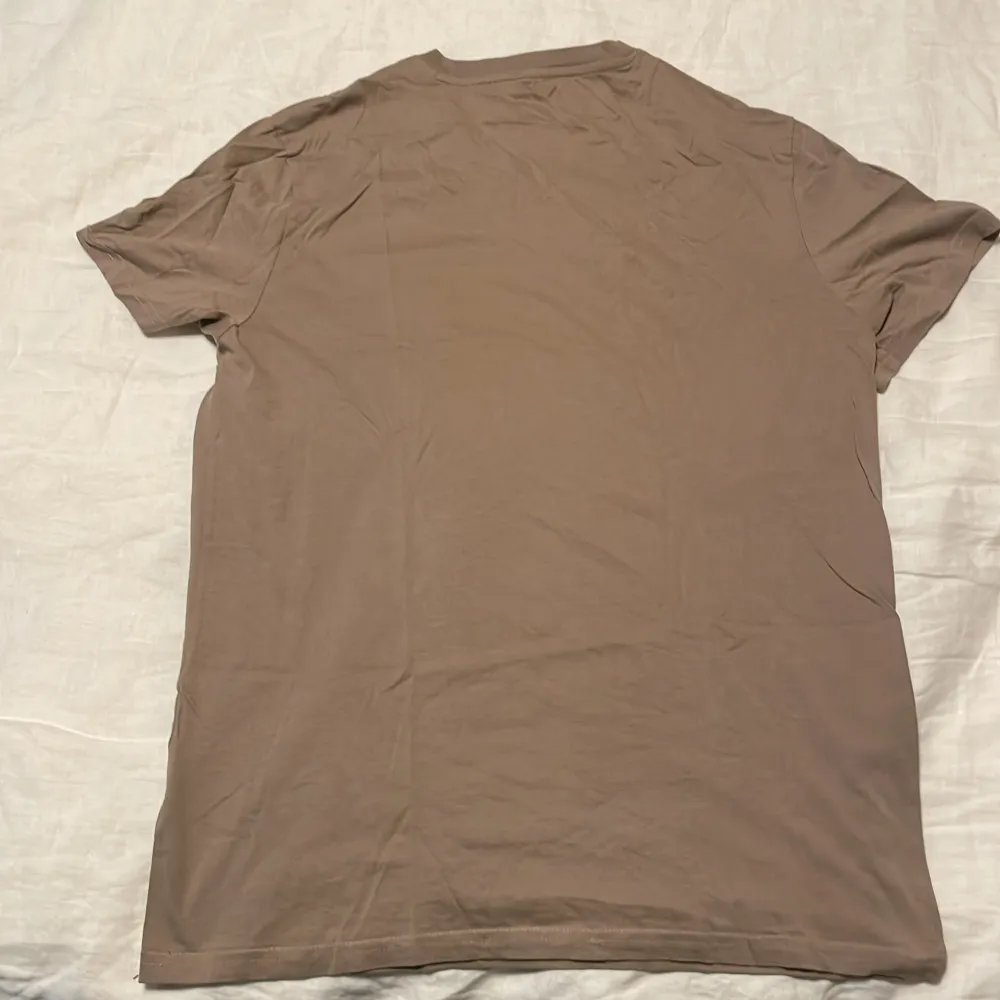 Säljer en enkel och stilren beige t-shirt i bomull. Den har en normal passform och korta ärmar, perfekt för vardagsbruk. T-shirten är i mycket bra skick och passar till alla tillfällen. Skön och lätt att matcha med andra plagg!. T-shirts.