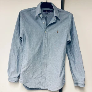 Blå skjorta från Ralph Lauren - Säljer en snygg blå skjorta från Ralph Lauren i slim fit. Skjortan har långa ärmar och en klassisk krage. Den är dekorerad med det ikoniska broderade logotypen på bröstet. Perfekt för både vardag och fest!