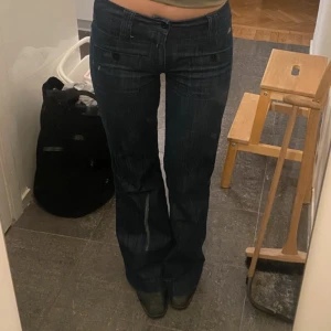 Mörkblå jeansbyxor - Säljer ett par mörkblå jeansbyxor i bootcut-stil. De har en lågmidjad passform och är perfekta för både vardag och fest. Byxorna har knappar framtill och är i bra skick. Perfekta för höst och vår!