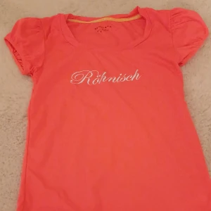 Rosa t-shirt från Röhnisch - Säljer en söt rosa t-shirt från Röhnisch. Den har korta ärmar med en liten puffdetalj och ett tryck med märkesnamnet på bröstet. Perfekt för en avslappnad dag eller lätt träning. Superbekväm och i bra skick!