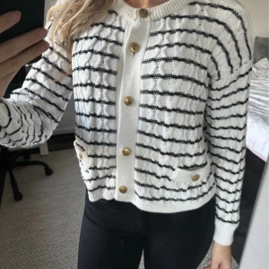 Vit och svart randig kofta med guldknappar - Säljer en superfin vit och svart randig kofta med snygga guldknappar. Den har två små fickor fram och är perfekt för både vardag och fest. Koftan är i mycket bra skick och passar perfekt till nu! Den är stickad och har långa ärmar för extra mysfaktor.