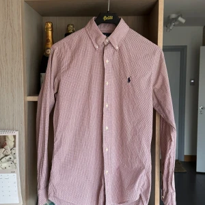 Rutig skjorta från Ralph Lauren - Storlek S - Säljer en klassisk rutig skjorta från Ralph Lauren i mycket bra skick. Skjortan är långärmad och har en snygg broderad logga på bröstet. Den är i en ljus röd och vit färgkombination, perfekt för både vardag och fest. Tillverkad i bomull för en bekväm passform. Passar perfekt till höst och vår!