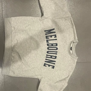 Grå sweatshirt från Gina Tricot - Säljer en snygg grå sweatshirt från Gina Tricot med texten 'Melbourne' i mörkblått på framsidan. Tröjan är i mycket bra skick och superbekväm att ha på! 🫶