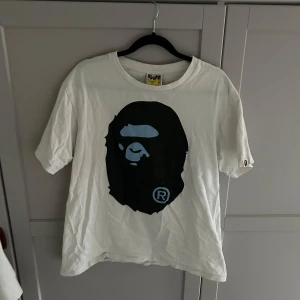 Vit t-shirt med tryck - Säljer en bape tshirt i storlek M. T-shirten är kortärmad och har en avslappnad passform. Perfekt för vardagsbruk eller som statement-plagg. Den är i bra skick men lite skrynklig men inget som inte försvinner i tvätten! Kan absolut ta byten!
