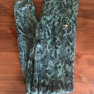 Mönstrade leggings från Gymshark - Säljer ett par snygga leggings från Gymshark i storlek S. De har ett coolt mönster i grönt och svart, perfekt för träning. Materialet är stretchigt och bekvämt, vilket gör dem idealiska för gymmet eller yoga. De är i mycket bra skick och redo för nya äventyr!