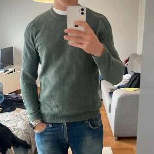 Grön stickad tröja - Säljer en snygg grön stickad tröja i bra skick. Perfekt för höst och vinter med sin mysiga och varma känsla. Tröjan har långa ärmar och en klassisk rund halsringning. Passar perfekt till jeans för en avslappnad stil.