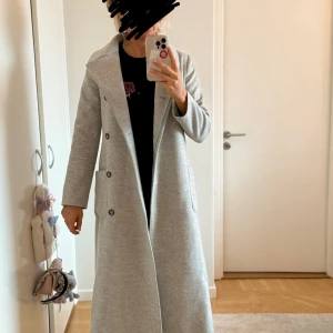 Grå ullkappa från Morris Lady - Säljer en elegant grå kappa från Morris Lady i storlek 36. Den är tillverkad av 100% ull och har en stilren design med knappar framtill och en slits bak. Perfekt för höst och vinter, och ger en klassisk look till vilken outfit som helst.