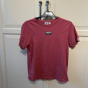 Rosa t-shirt från Adidas - Säljer en snygg stor rosa t-shirt från Adidas i storlek S. Den har en klassisk design med korta ärmar och en liten logga på bröstet. Perfekt för vardagsbruk eller träning. Materialet är mjukt och bekvämt, vilket gör den idealisk för både träning och vardags. 