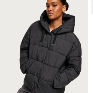 Svart pufferjacka - Säljer en svart pufferjacka i mycket bra skick. Den är perfekt för kalla dagar med sin varma och vadderade design. Jackan har en stor huva och långa ärmar, vilket gör den idealisk för vinter och höst. Den har en dragkedja framtill och är i en normal passform.