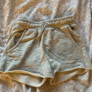 Grå frottéshorts - Mysiga grå shorts i frotté med elastisk midja och snörning. Perfekta för en avslappnad dag hemma eller en promenad i parken. De har en loose passform och praktiska fickor på sidorna. Superbekväma och stilrena!