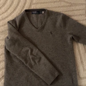 Grå merinoull tröja från Polo Ralph Lauren - Säljer en stilren grå tröja från Polo Ralph Lauren i storlek M/S. Tröjan är i mycket bra skick och har en klassisk v-ringning. Perfekt för både höst och vinter, och den är supermjuk och bekväm. Passar till alla tillfällen! Köpt från ralph laurens hemsida för 2300 SEK