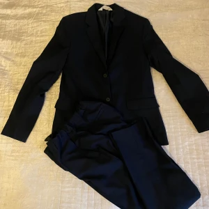 Kostym barn/ungdom - Mörkblå kostym från H&M. Kavaj med två knappar och knappar vid ärmslut. Byxorna har reglerbar resår i midjan. Strl 164 Nypris 599