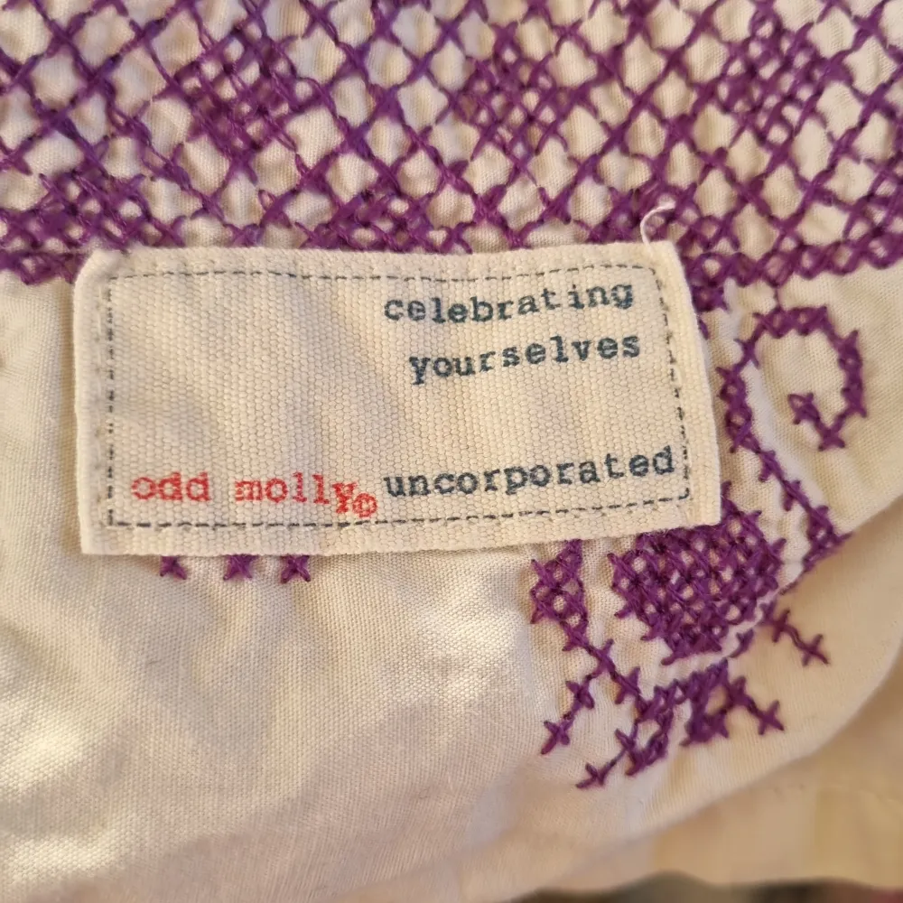 Säljer en unik blus från Odd Molly i mycket bra skick. Den har ett vackert lila mönster på vit bakgrund med röda detaljer och ett brett midjeband. Klänningen har volanger och en knytning i midjan för en fin passform. Perfekt för vår och sommar!. Blusar.