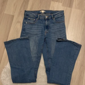 Blå jeans från Gina tricot  - Säljer ett par snygga blå jeans från Gina tricot. Den har knappar på bakfickorna. Perfekta för vardagsbruk och kan enkelt matchas med olika toppar. Passar både till skolan och fritiden!