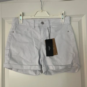 Vita shorts från vero Moda - Säljer ett par snygga vita shorts från vero moda i nytt skick. De är högmidjade med en klassisk design och har uppvikta benslut. Perfekta för sommardagar och kan enkelt matchas med olika toppar. Storlek dam S.