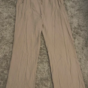 Beige linnebyxor - Säljer ett par bekväma beige byxor. De har en loose passform och är perfekta för en avslappnad stil. Byxorna har en elastisk midja för extra komfort.