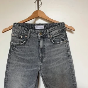 Grå jeans från Zara - Säljer ett par snygga grå jeans från Zara. De är mid waist och har en klassisk femficksdesign med knapp och dragkedja fram. Jeansen har en straight passform med slits vid fötterna. De är i bra skick och redo för en ny ägare! Lite slitna längst ner.