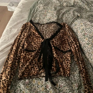 Leopardmönstrad långärmad topp med knytband - Säljer en supercool leopardmönstrad topp med långa ärmar. Den har snygga svarta knytband framtill och en fin spetsdetalj längs kanterna. Perfekt för en utekväll eller när du vill sticka ut lite extra. 🐆✨