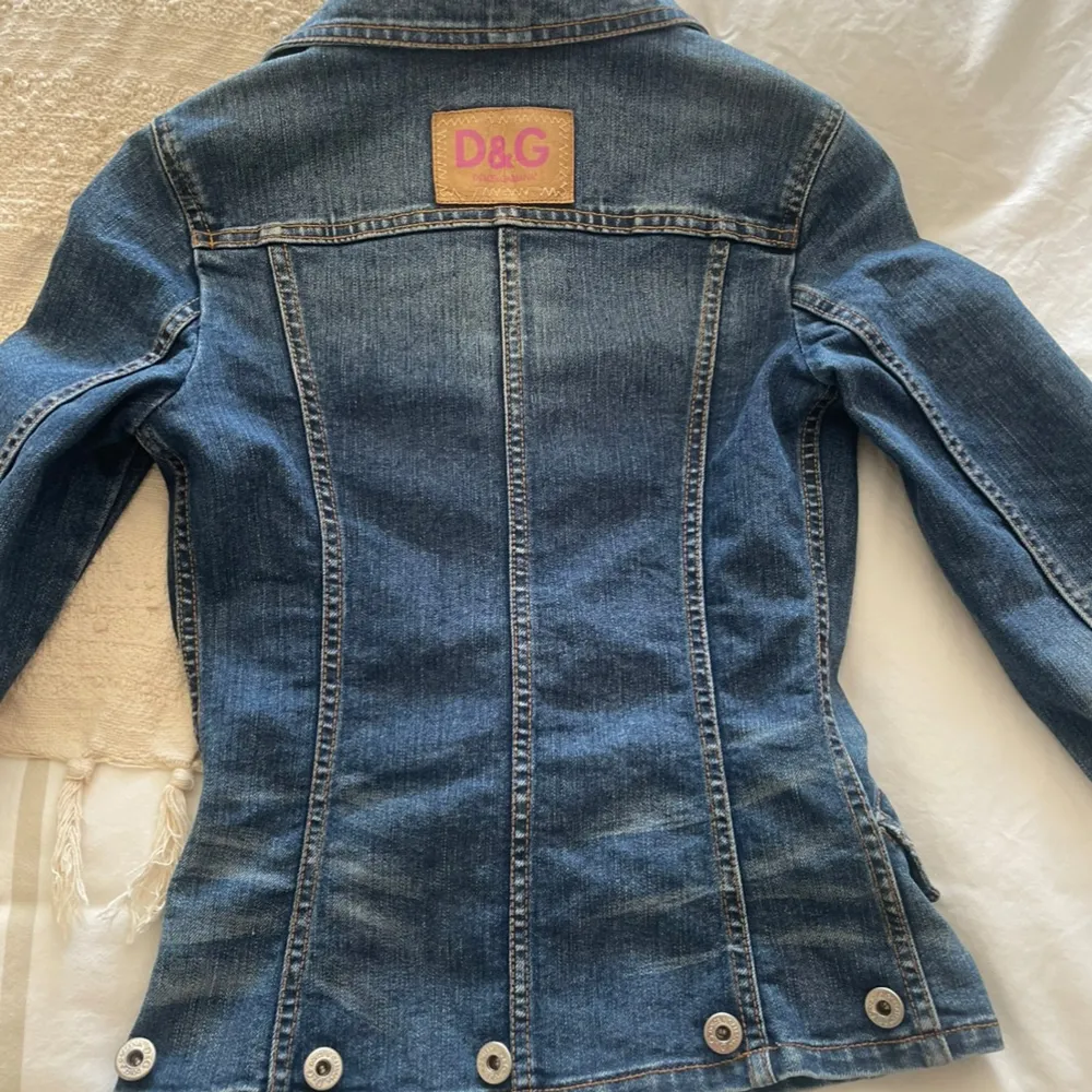 Säljer en snygg jeansjacka från D&G i klassisk blå denim. Jackan har en figursydd passform. Mått midja som bild 5, är  33 cm. Mått från armhåla till handled är  49 cm. Mått över byst  38cm. Står ingen storlek så XS är min gissning. . Jackor.