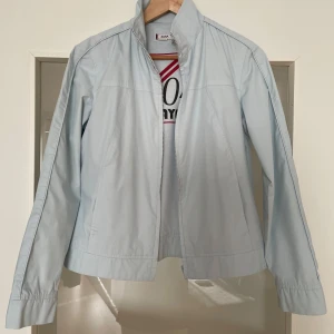 Ljusblå jacka från Zara TRF - Säljer en stilren ljusblå jacka från Zara TRF i storlek M. Jackan är tillverkad av en blandning av polyester och bomull, vilket gör den både bekväm och lätt. Den har en enkel design med långa ärmar och en dragkedja framtill. Perfekt för vår och sommar!