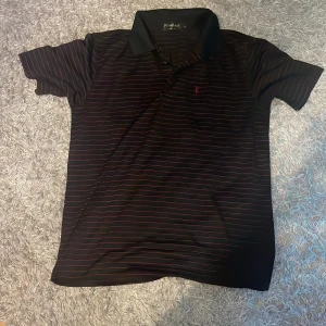 Svart och röd randig pikétröja från Yves Saint Laurent - Snygg svart silk pikétröja från Yves Saint Laurent med röda ränder och broderad logga på bröstet. Jätte bra för sommaren då den är luftig. Storlek L men sitter som S-M. Skick 7/10 men är inte för sliten, skriv om du undrar något eller har prisförslag!!