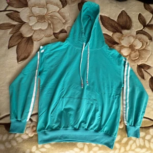 Turkos hoodie med vita ränder - Mycket fint skick  - Turkos hoodie. Vita ränder längs ärmarna. Texten ”NICE” på snörena. Stor ficka. Luftig. Normalstor luva. Märket är okänt. Osäker på vilket material den är gjord av. Höger snöre har en söm som sticker ut, finns sömmar på baksida och insida (se bilder) som också är lösa. Använd 2 gånger. Storlek: Okänd, sitter bra på M. Skick: Mycket fint. Nypris: Ca 299 kr. 