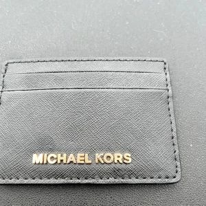 Svart plånbok från Michael Kors - Snygg och stilren svart plånbok från Michael Kors i skinn. Perfekt för att hålla dina kort organiserade med flera kortfack. Den kompakta designen gör den lätt att bära med sig.