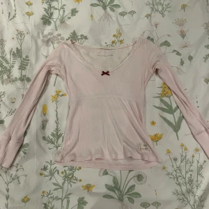 Rosa långärmad topp från Odd Molly - Söt ljusrosa ribbad topp med spetskant och en liten röd rosett vid halsringningen. Fint skick, passar S-M