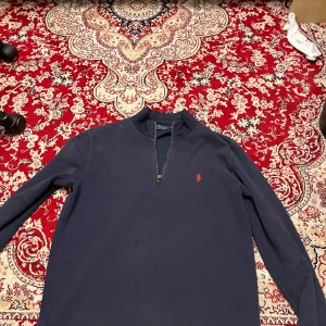 Mörkblå tröja från Polo Ralph Lauren - Säljer en stilren mörkblå tröja från Polo Ralph Lauren med dragkedja och röd logga på bröstet. Perfekt för en avslappnad och snygg look.