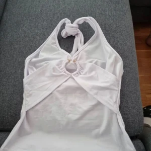 Vit halterneck topp - Snygg vit halterneck topp med knytning i nacken och dekorativ ringdetalj framtill. Perfekt för varma sommardagar.