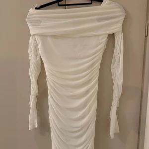 Vit offshoulder klänning - Elegant vit offshoulder med överlappande tyg, klänning med rynkade detaljer med slits i slutet på ärmarna. 