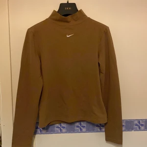 Brun polotröja från Nike - Säljer en snygg brun polotröja från Nike med en liten vit logga på bröstet. Tröjan har långa ärmar och är perfekt för en sportig look. Passar bra till både jeans och träningsbyxor.