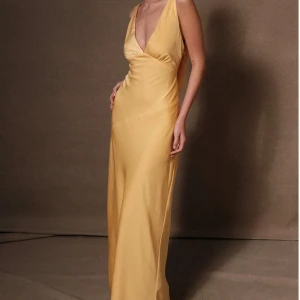 Gul långklänning med öppen rygg - Elegant gul långklänning med djup v-ringning och öppen rygg. Klänningen har en smickrande passform och är perfekt för speciella tillfällen. Tillverkad i ett mjukt och följsamt material som ger en lyxig känsla. Nypris 100€