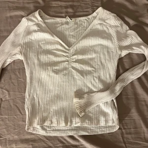 Vit ribbad tröja med v-ringning - Säljer en stilren vit ribbad tröja med v-ringning och långa ärmar. Perfekt för lager-på-lager eller som den är. Enkel och snygg design som passar till det mesta.