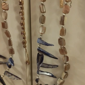 Unika halsband med pärlor och blå detaljer - Två vackra halsband med unika pärlor i beige och blå nyanser. Det ena halsbandet har spetsiga blå detaljer som ger en modern touch. Perfekt för att lyfta en outfit med lite extra stil.