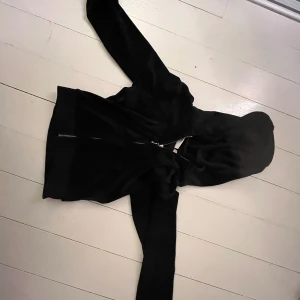 Svart hoodie med dragkedja - Snygg svart hoodie med dragkedja och huva. Perfekt för en avslappnad stil. Den har en diskret logga på bröstet och är tillverkad i ett mjukt material.