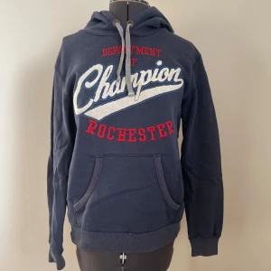 Mörkblå hoodie från Champion - Mörkblå hoodie från Champion med texten 'Department of Champion Rochester' i vitt och rött.