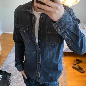 Nudie Jeansskjorta - Säljer denna riktigt schyssta jeansskjorta från nudie jeans. Riktigt bra kvalité på denimtyget på denna skjorta, då nudie gör bra grejer. Lite slitningar fram mitt på skjortan som jag antar ska vara där. Klassisk blå färg, passar dig som har storlek M bra! Skriv jättegärna om du har frågor eller prisförslag!