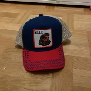 Revenite keps limeted edition  - Snygg keps med blå framsida och röd skärm. Baktill finns ett beige nät för ventilation. Framsidan pryds av en broderad patch med text och bild. Perfekt för en avslappnad stil.