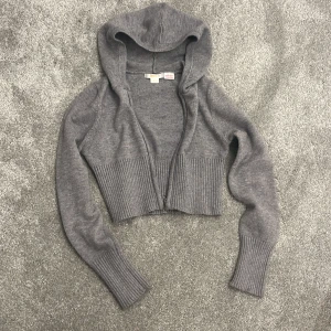 Grå croppad hoodie från Gina Tricot - Säljer en snygg grå croppad hoodie från Gina Tricot. Den har en dragkedja framtill och långa ärmar med ribbade muddar. Perfekt för en avslappnad stil. 