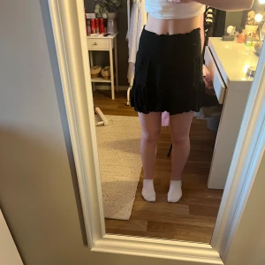 Svart kjol med volangdetaljer - Snygg svart kortkjol med volangdetaljer. Kjolen har en elastisk midja för bekväm passform. Från lager 157, storlek S och knappt använd.